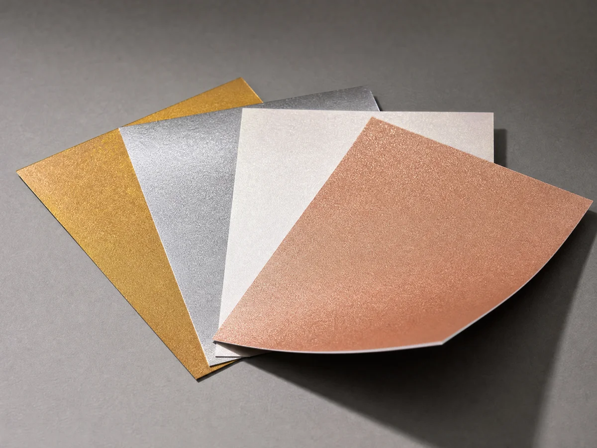 Selection of metallic and pearlescent paper swatches in gold silver and pearl white showing iridescent shimmer under lighting
