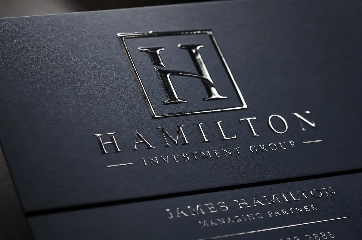 Close-up detail of spot UV coating on a business card — glossy raised logo contrasting against a matte background