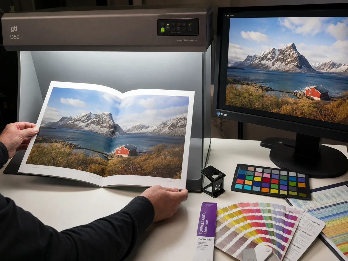 Artist reviewing color proof under calibrated lighting, comparing printed spread against calibrated monitor display