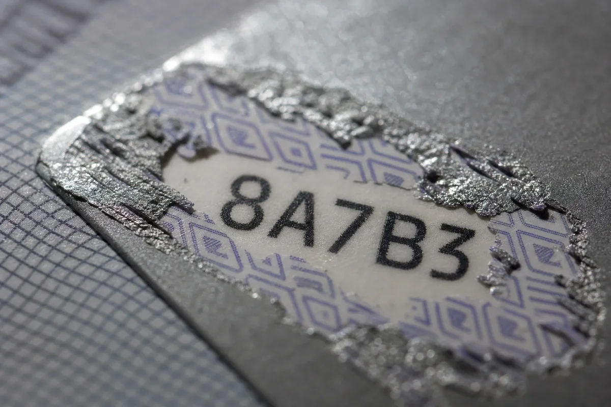 Close-up of scratch off card printing showing silver scratch panel, security pattern layer, and revealed code underneath