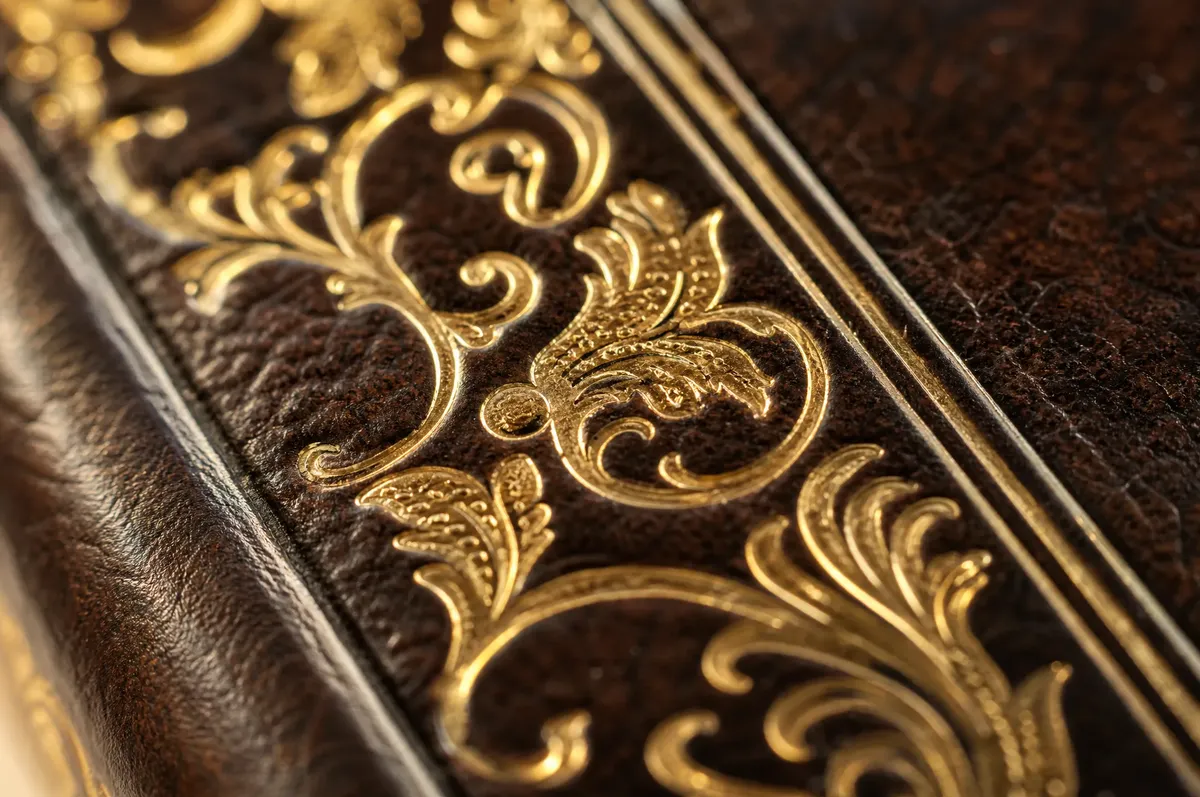 Close-up of gold foil stamping detail on a dark leather book cover with embossed title lettering
